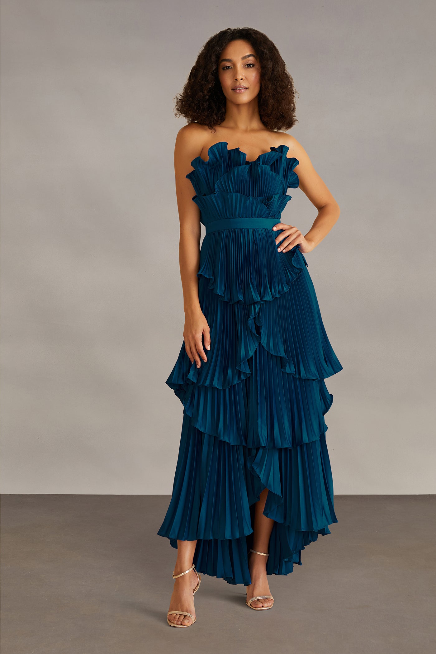 Woman wearing a strapless, ruffled teal dress against a neutral background
