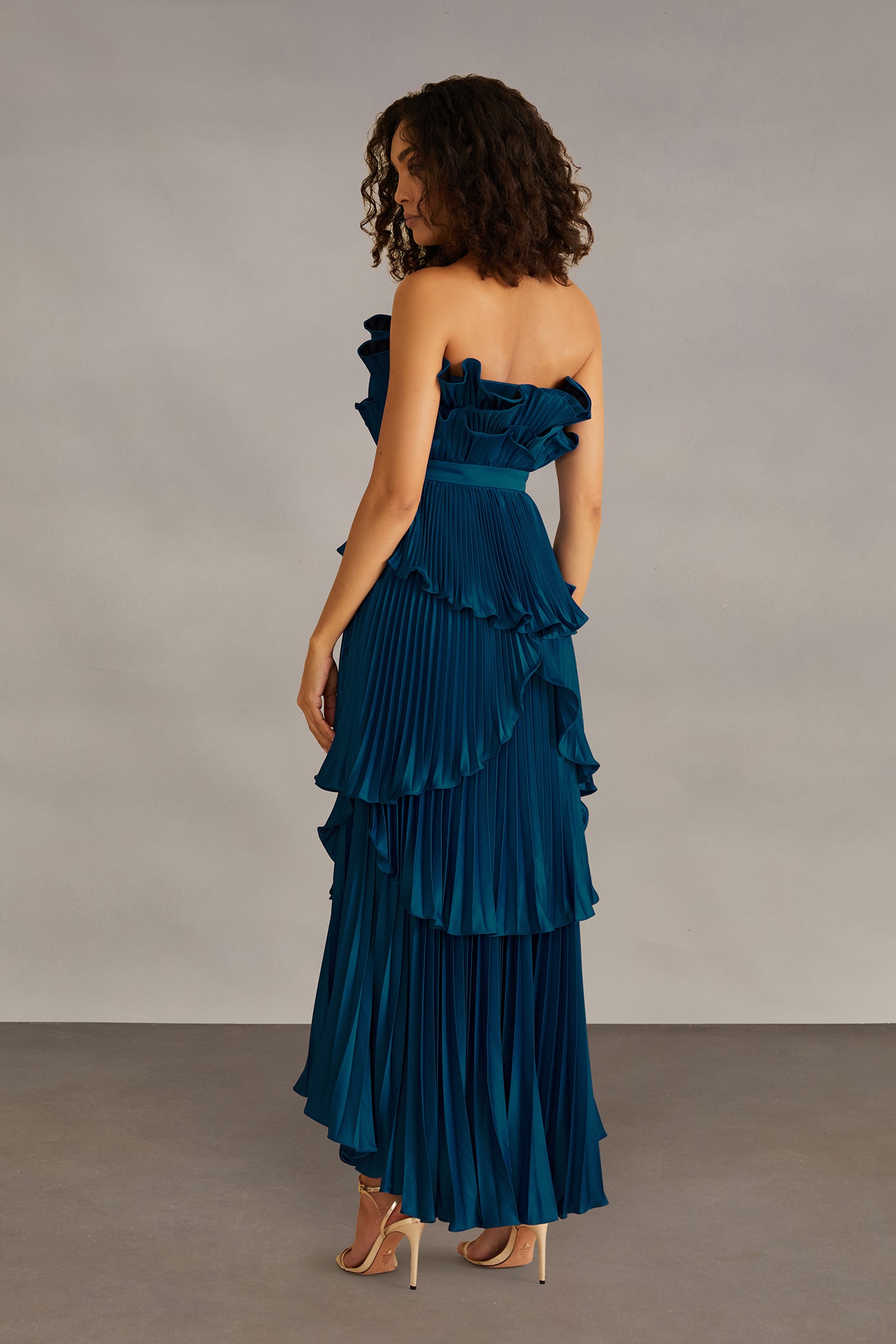 Woman wearing a teal strapless ruffled gown against a neutral background