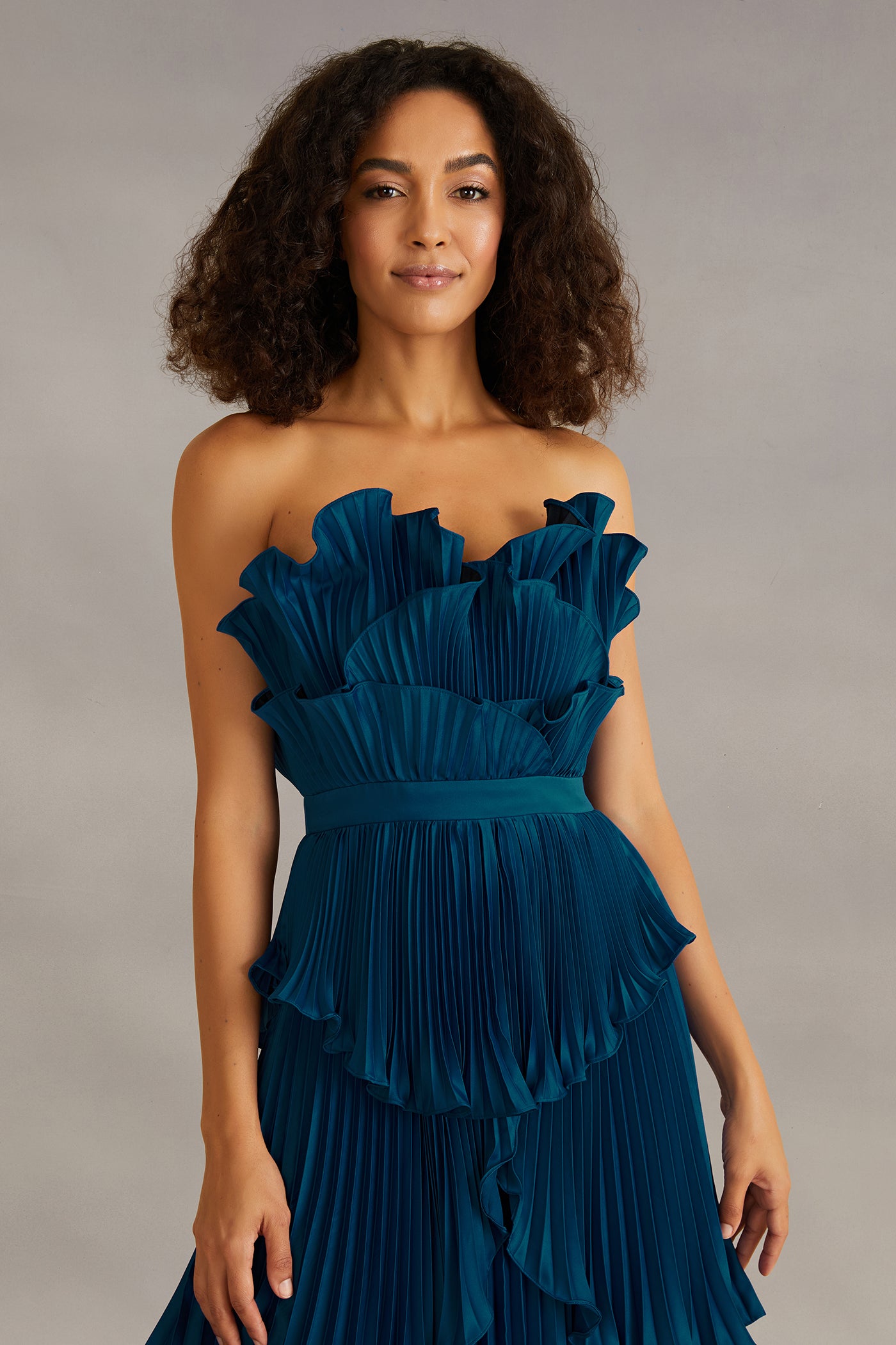 Woman wearing a blue strapless dress with ruffled layers against a gray background