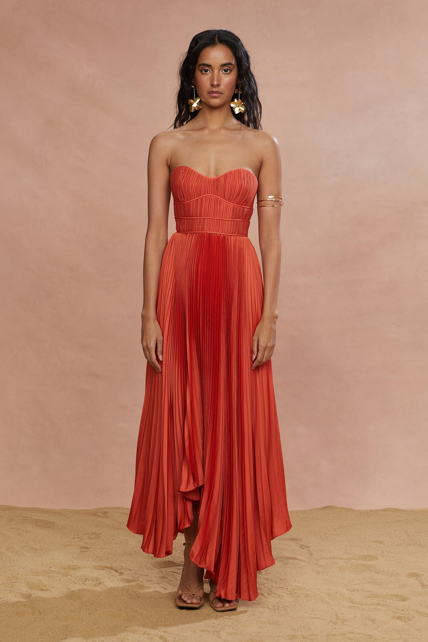 A woman wearing a red strapless midi dress with pleats and a sweetheart neckline.