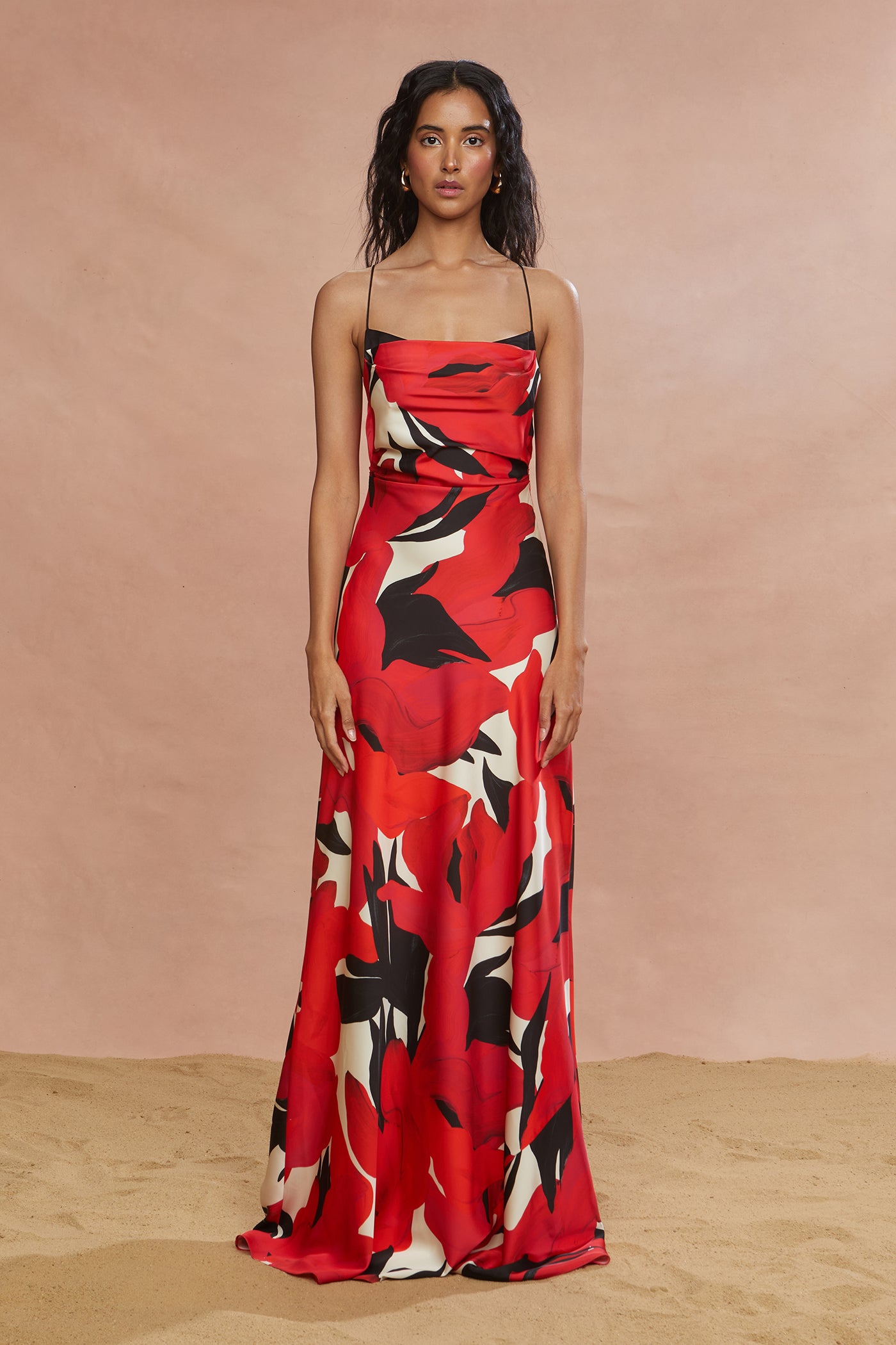 A woman modeling a red maxi dress with a floral pattern, featuring a fitted waist and spaghetti straps.