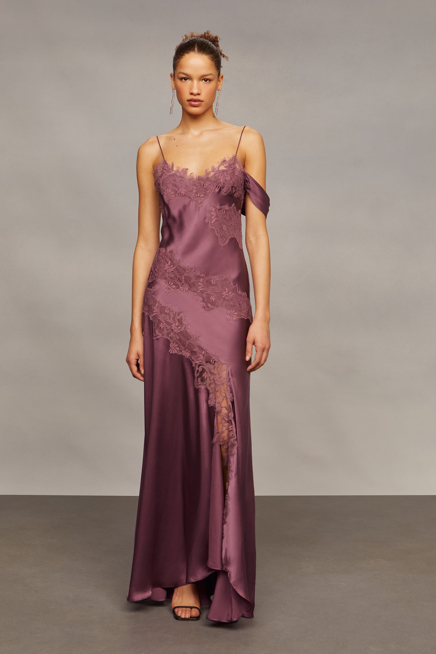 Woman wearing a long, elegant purple dress with lace details against a plain background