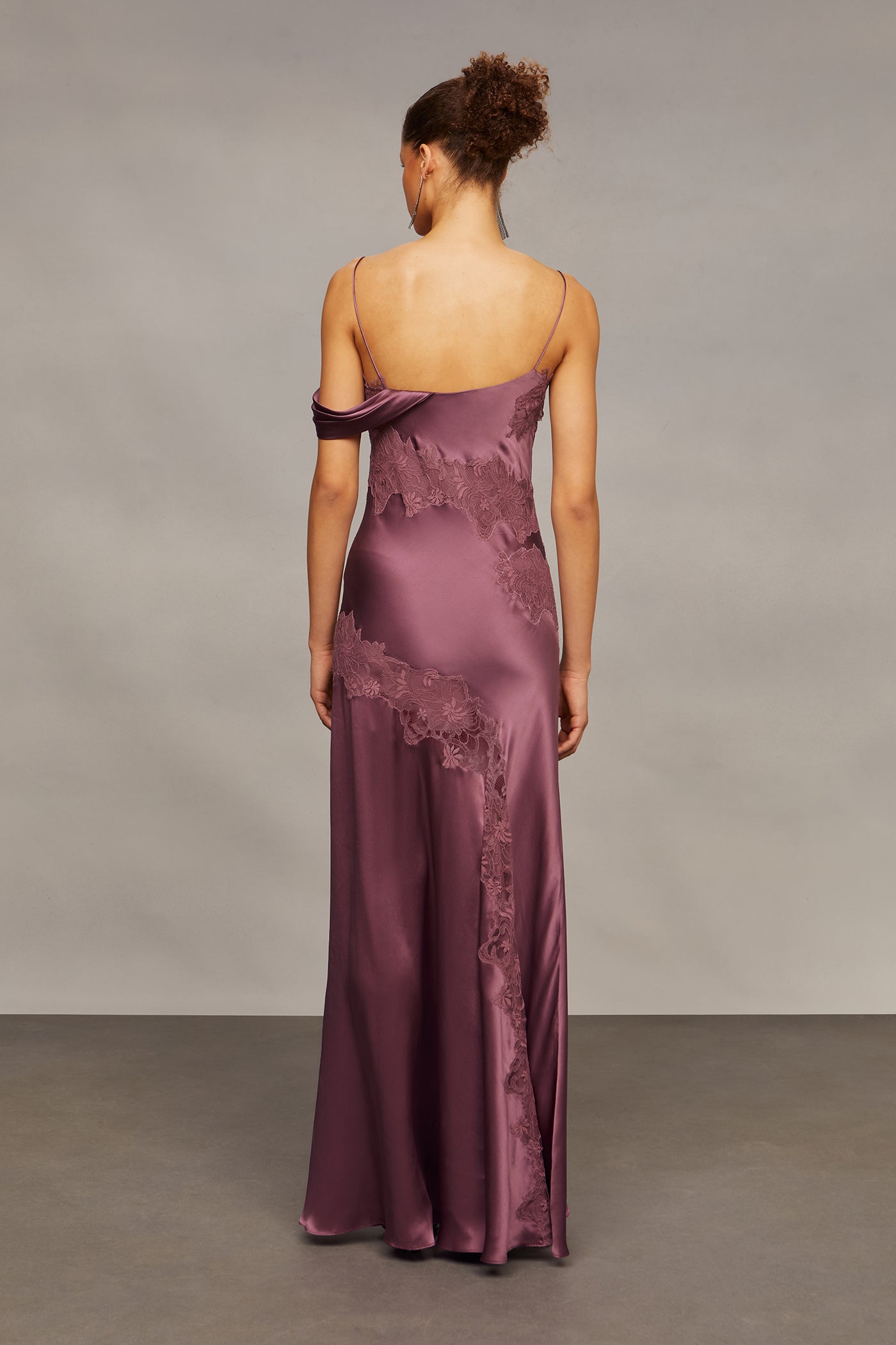 Woman wearing a long, elegant purple gown with lace details against a neutral background