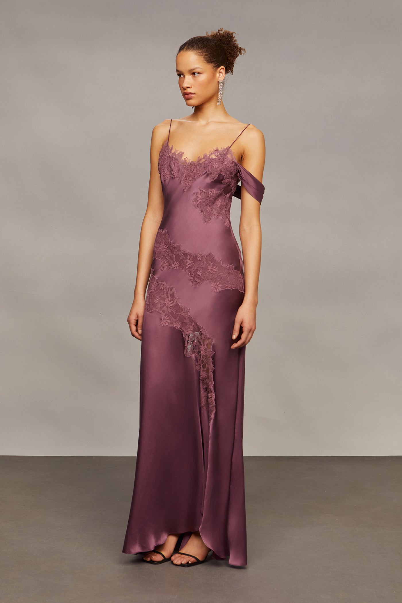 Woman wearing a long purple dress with lace details against a neutral background