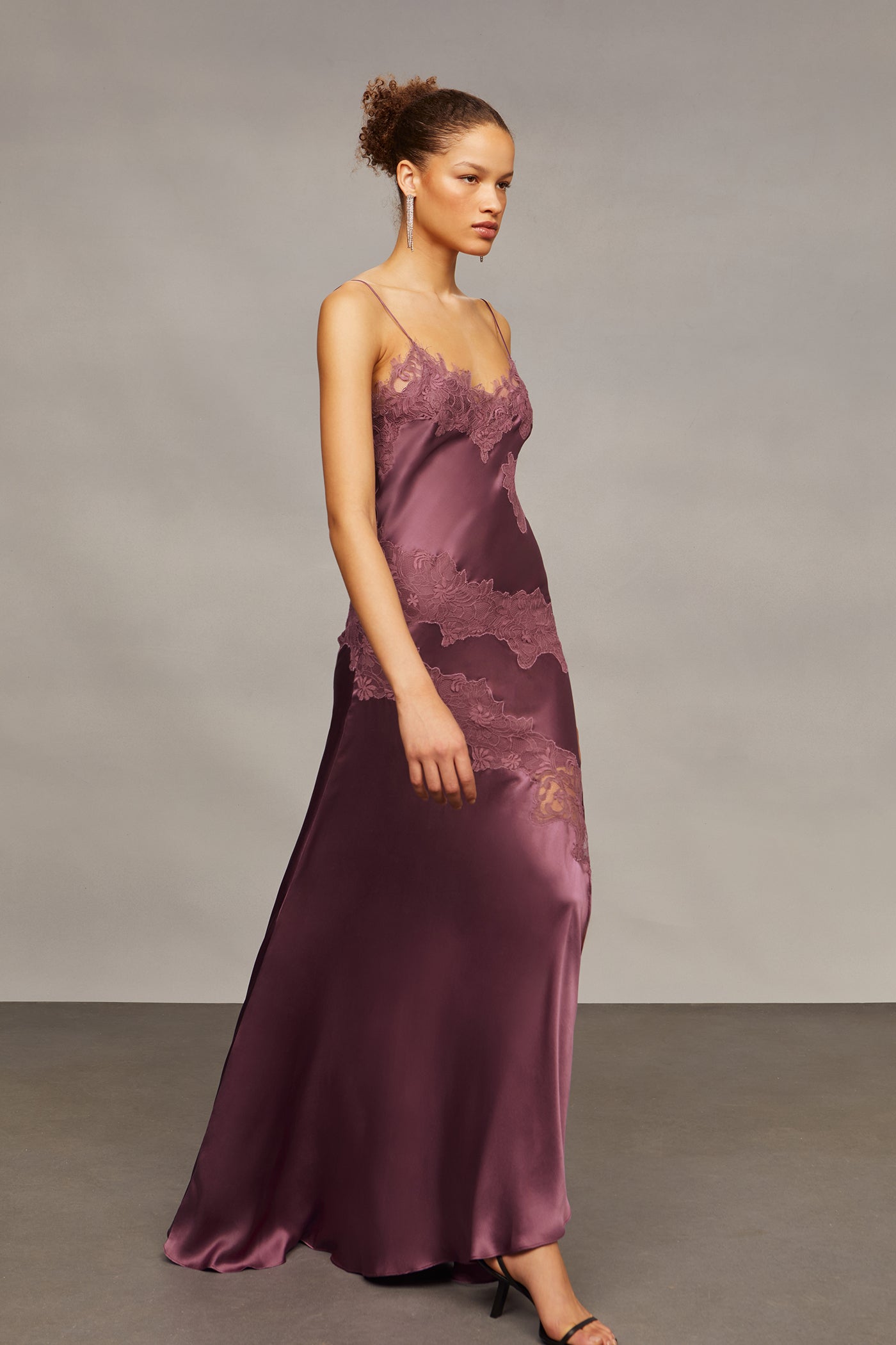 Woman wearing a purple lace evening gown against a plain background