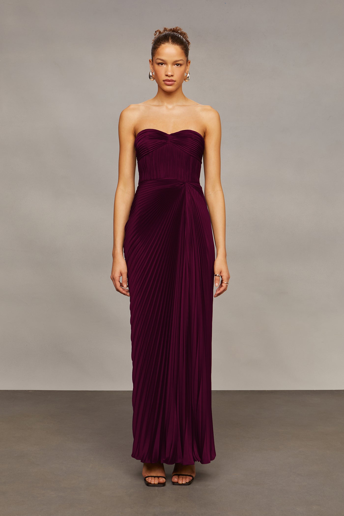 Woman wearing a strapless burgundy gown against a neutral background