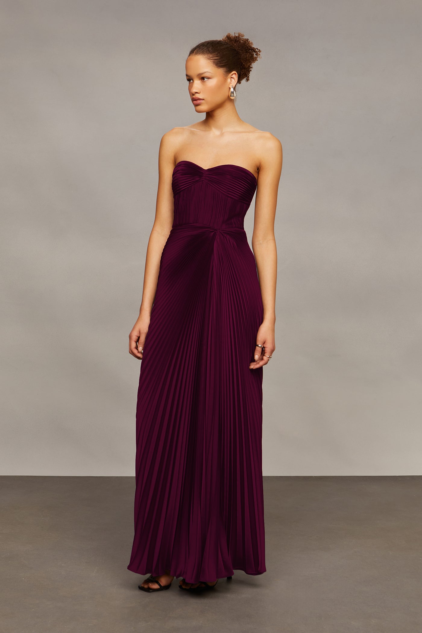Woman wearing a strapless burgundy gown against a neutral background