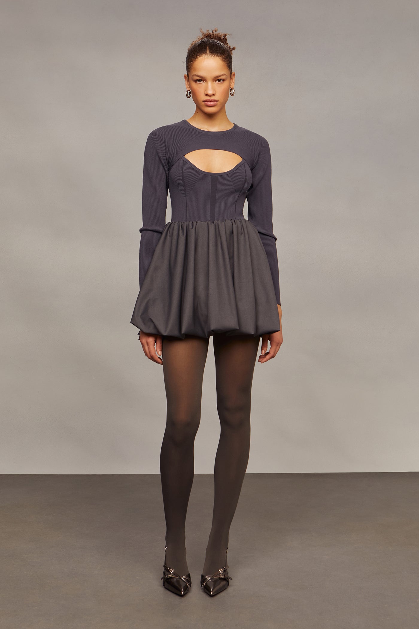 Woman wearing a dark gray dress with cut-out design on a plain background