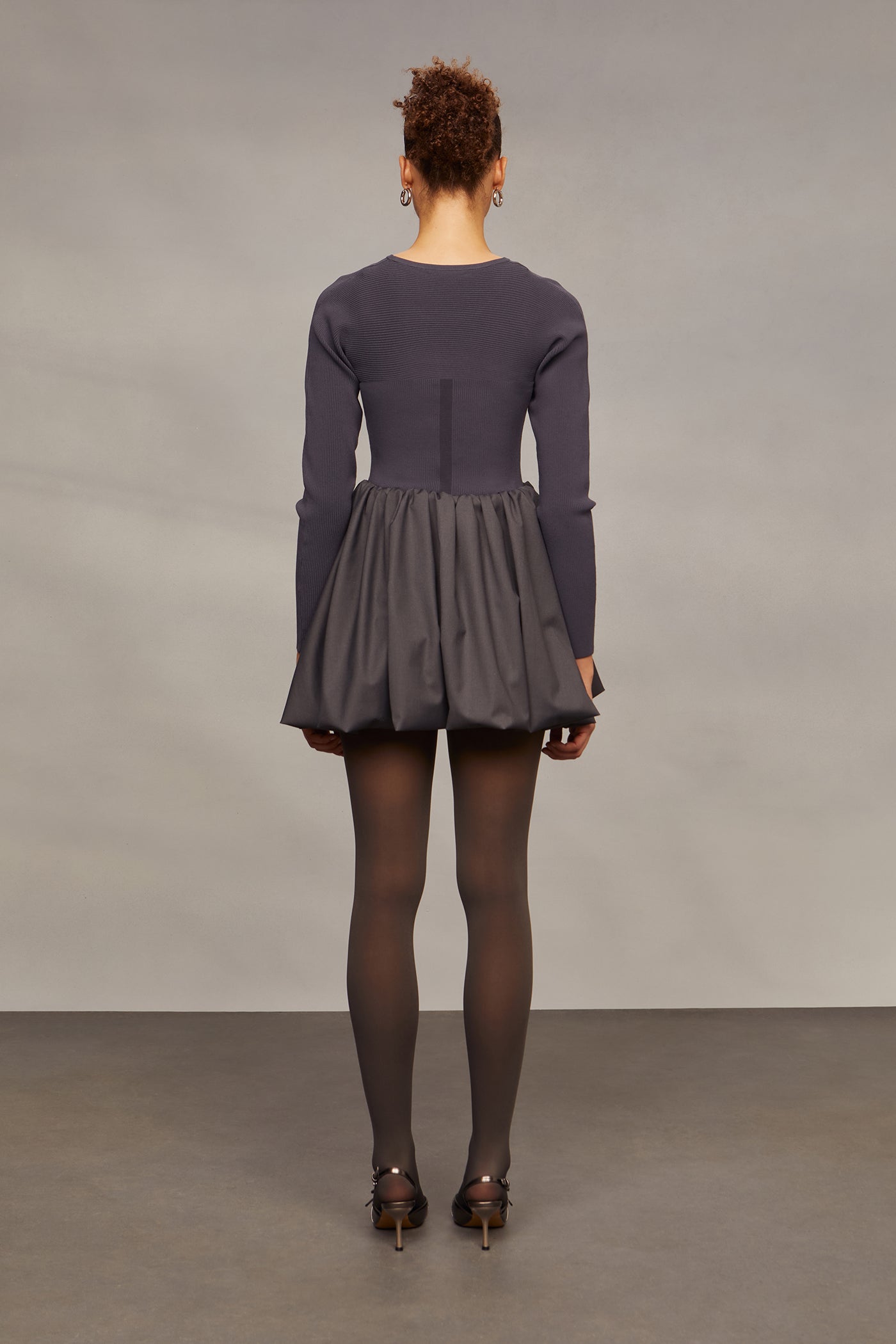 Person wearing a long-sleeve top and pleated skirt against a plain background