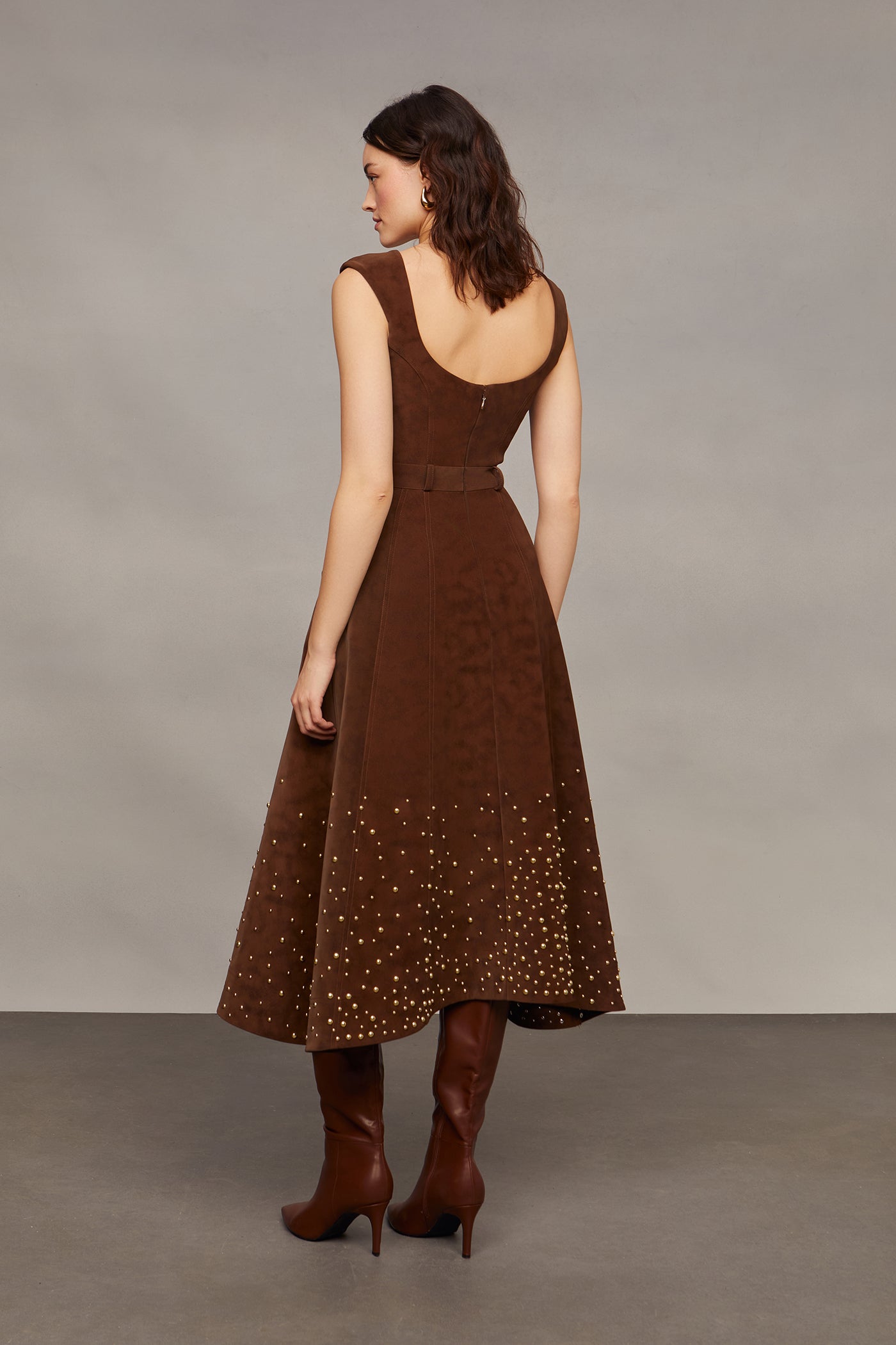 Woman wearing a brown studded dress against a plain background