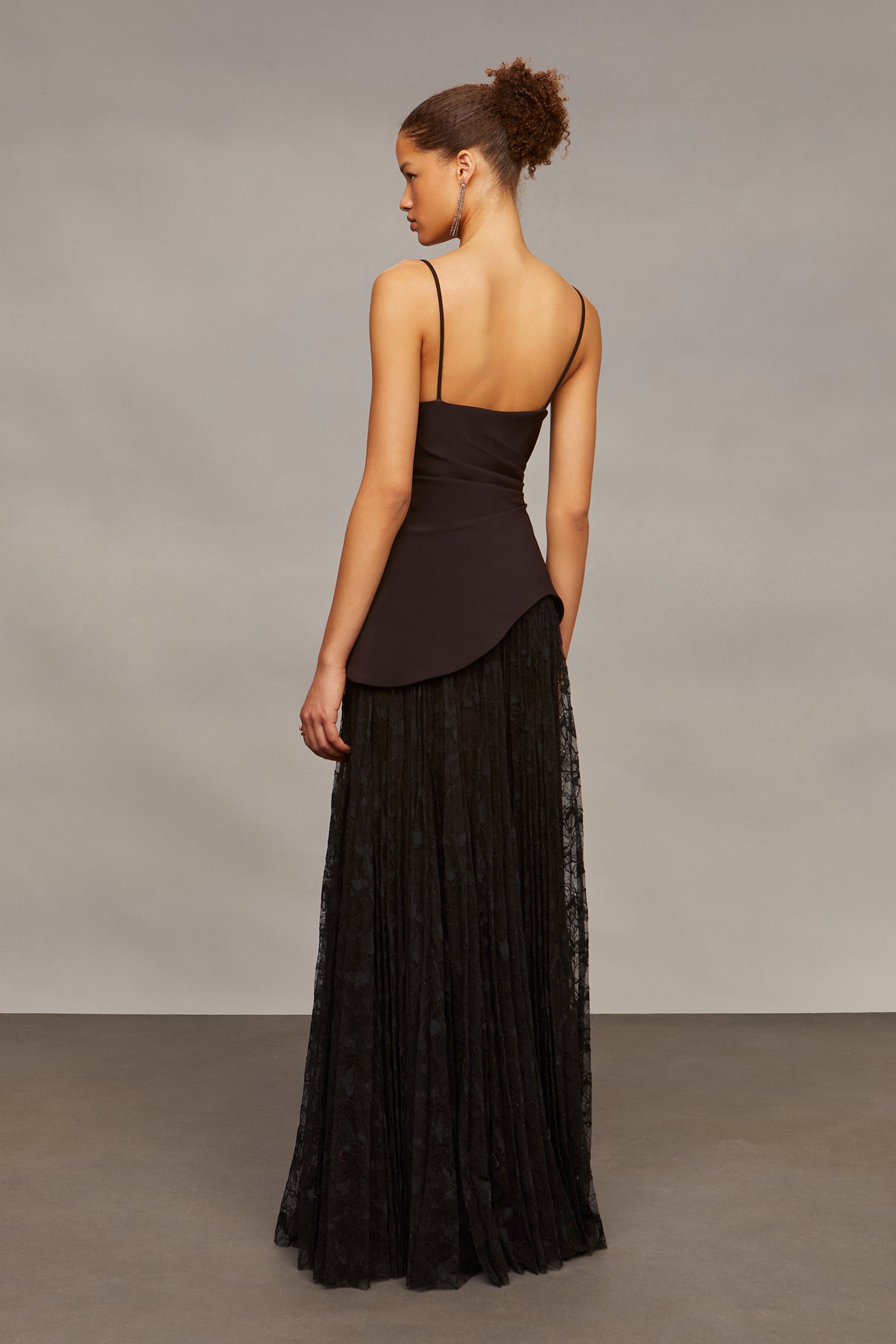 Woman wearing a black dress with a sheer overlay against a neutral background