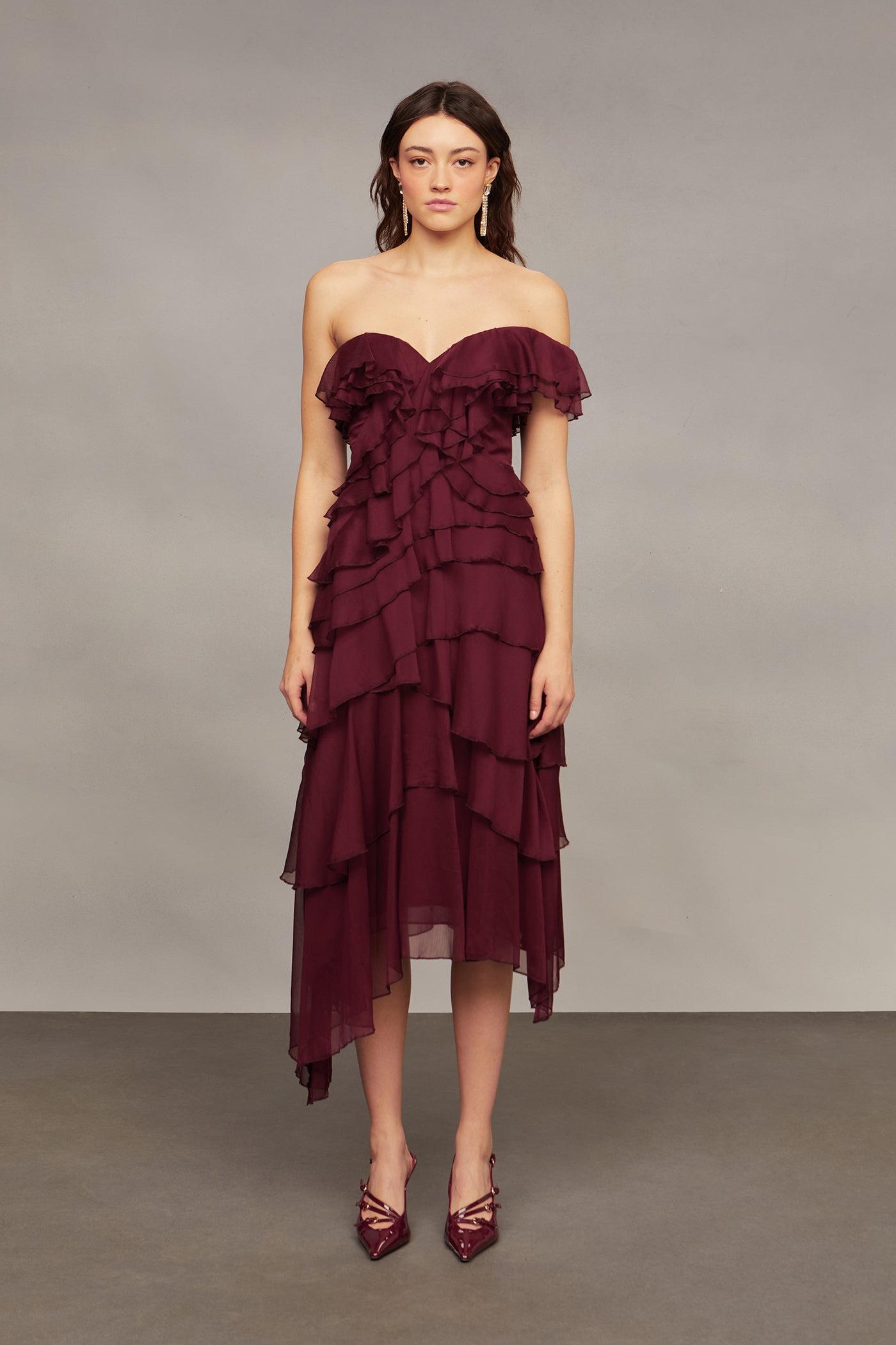 Woman wearing a burgundy strapless dress with ruffled layers against a neutral background