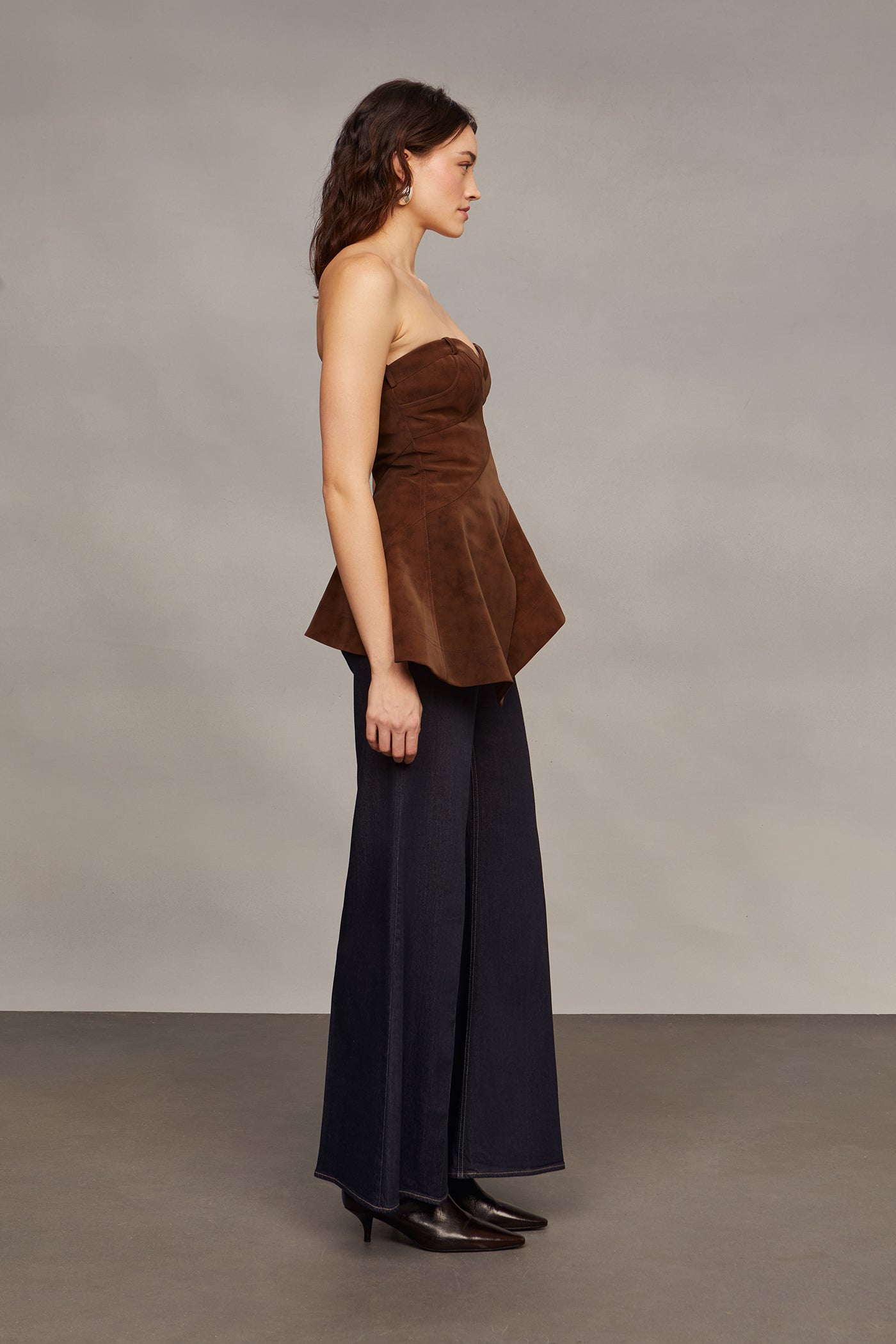 Woman wearing a brown strapless top and blue flared pants against a plain background