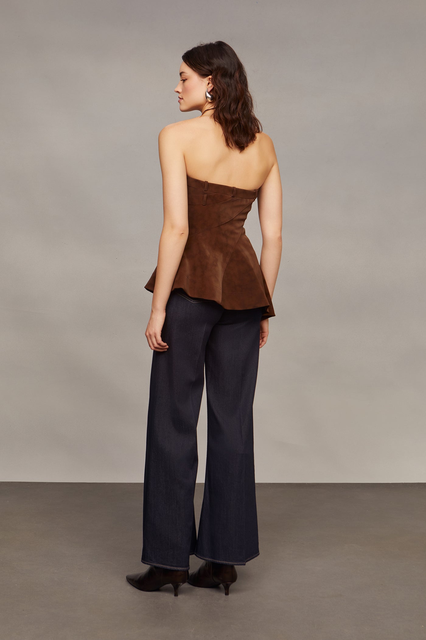 Woman wearing a brown strapless top and blue flared pants against a plain background