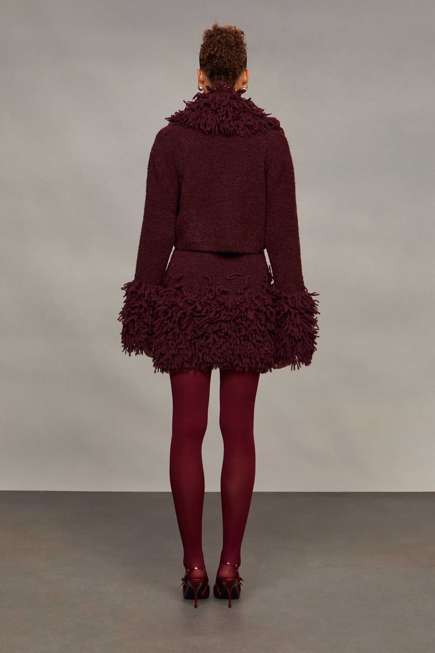 Person wearing a burgundy textured outfit with matching tights against a plain background