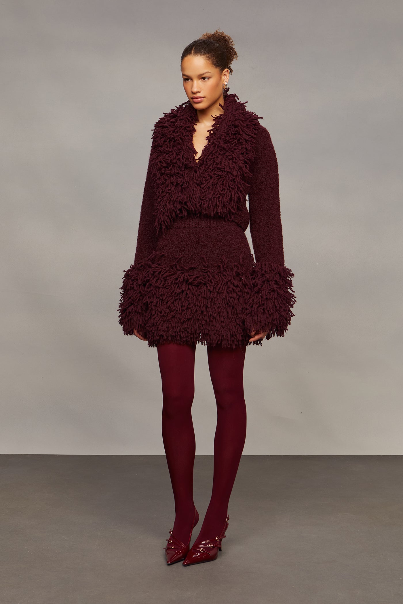 Woman wearing a burgundy textured outfit with matching shoes on a gray background