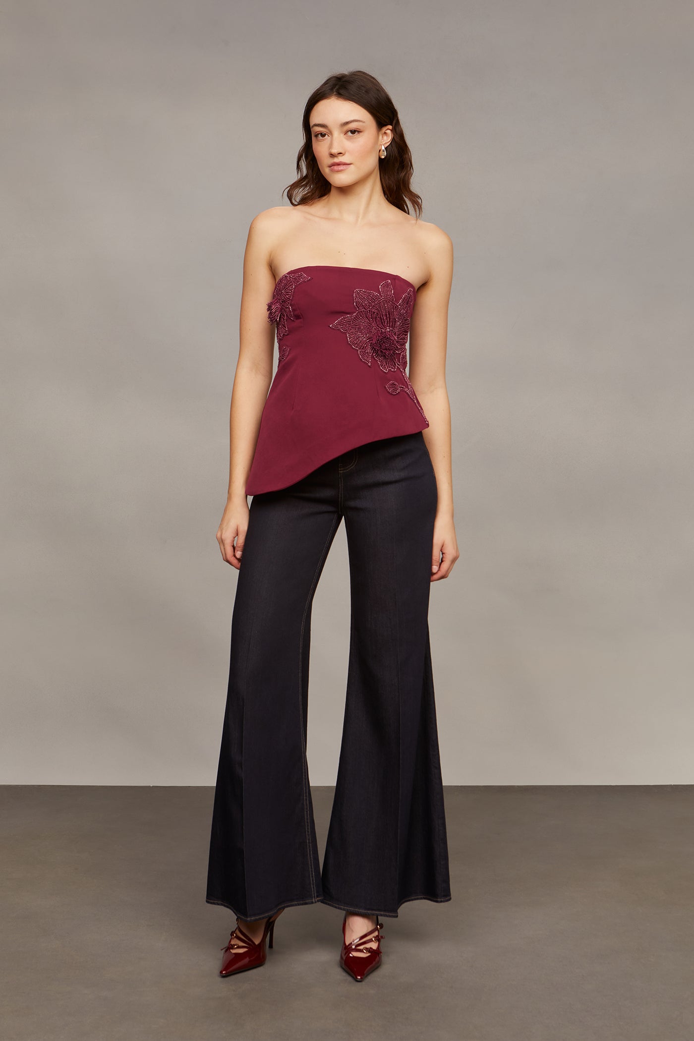 Woman wearing a strapless burgundy top and black pants against a neutral background