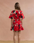 Woman wearing a red floral dress against a beige background