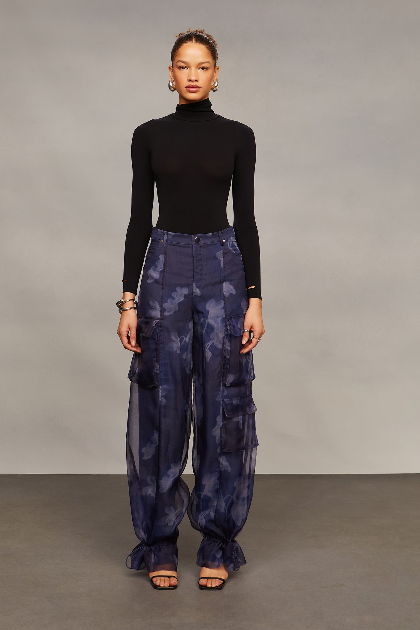 Model wearing a black turtleneck and blue patterned pants against a gray background