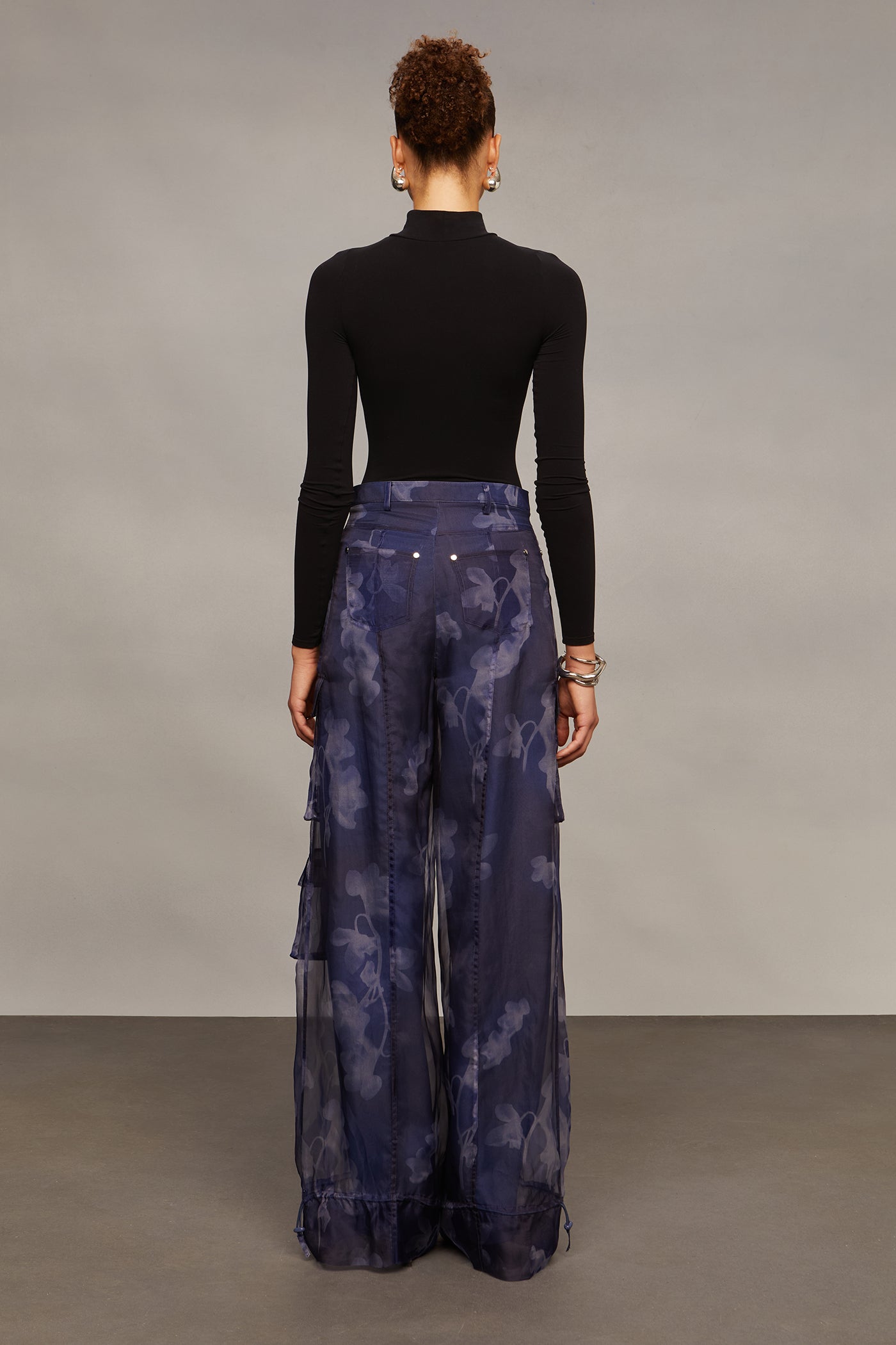Person wearing a black turtleneck and blue tie-dye pants against a gray background