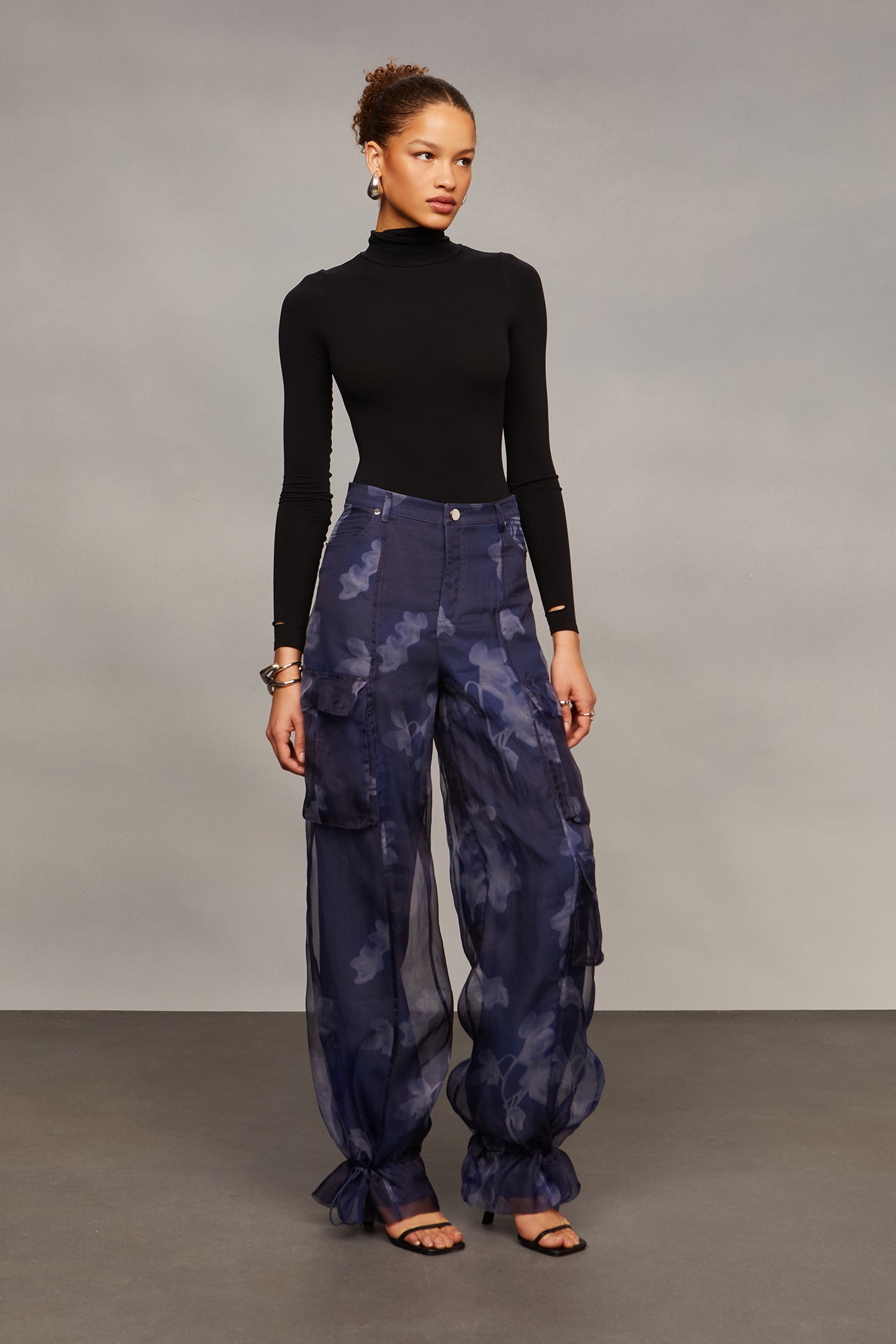 Woman wearing a black turtleneck and blue tie-dye cargo pants against a gray background