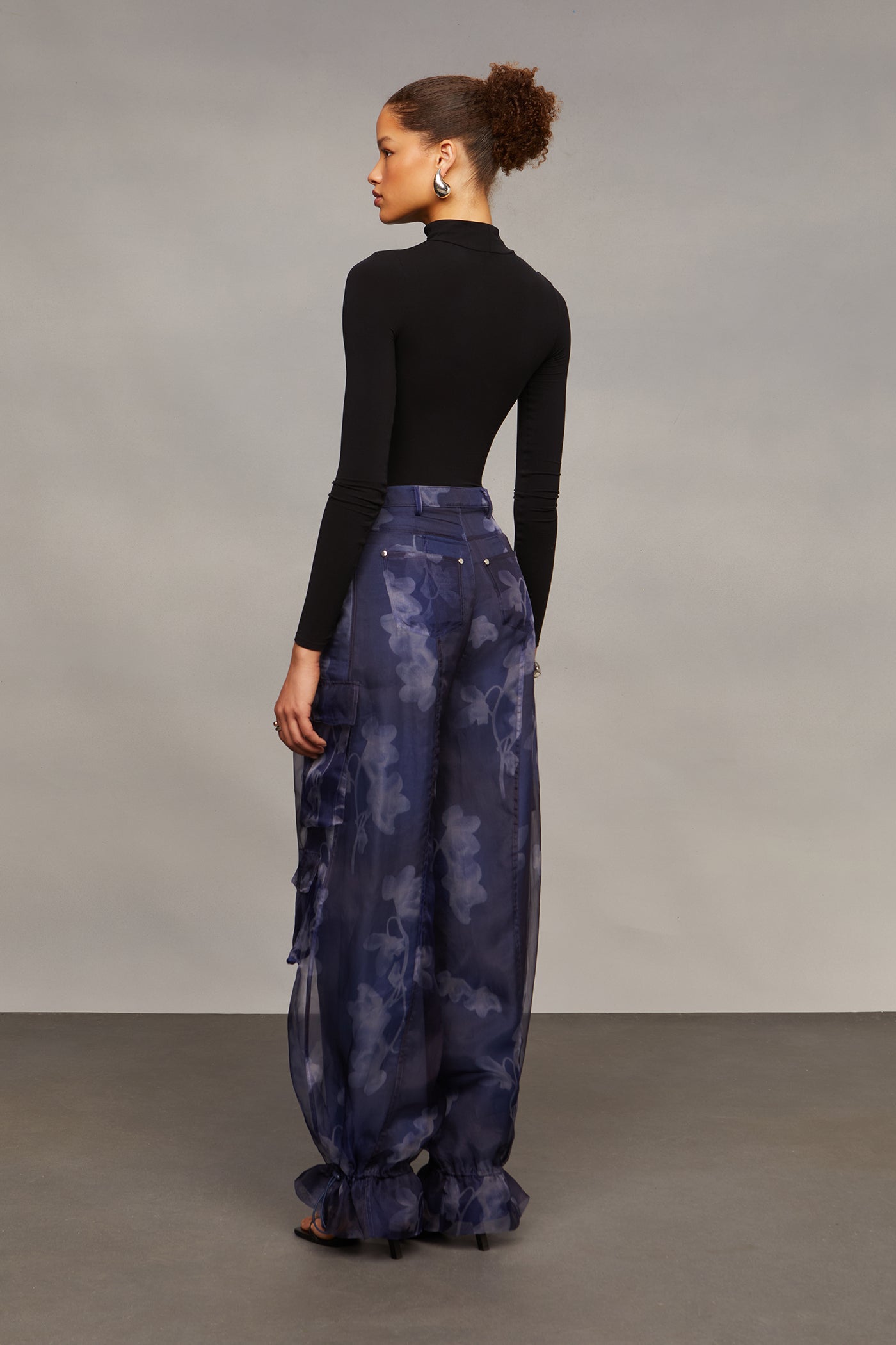 Woman wearing a black top and blue floral pants against a gray background