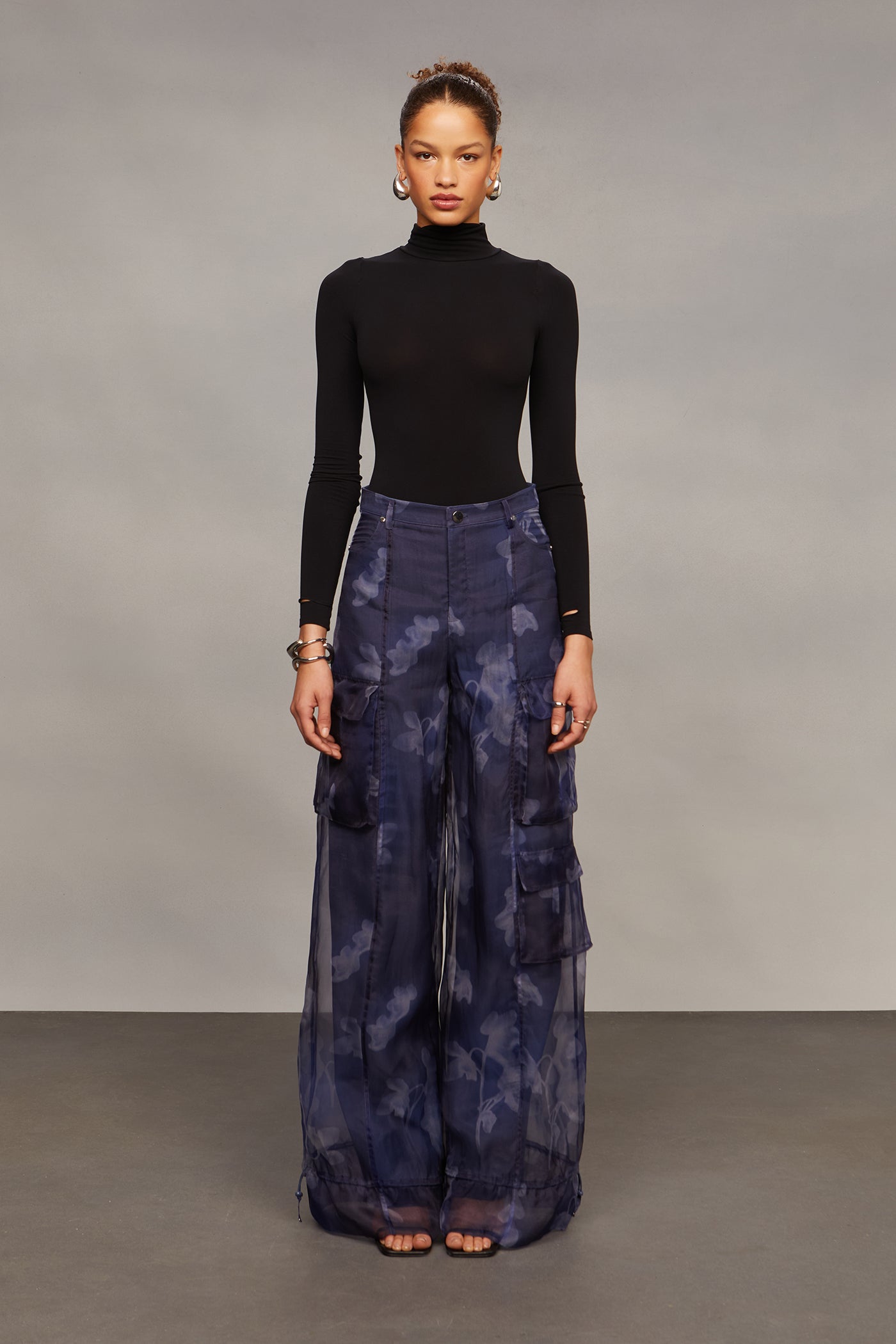 Model wearing a black turtleneck and blue patterned pants against a gray background