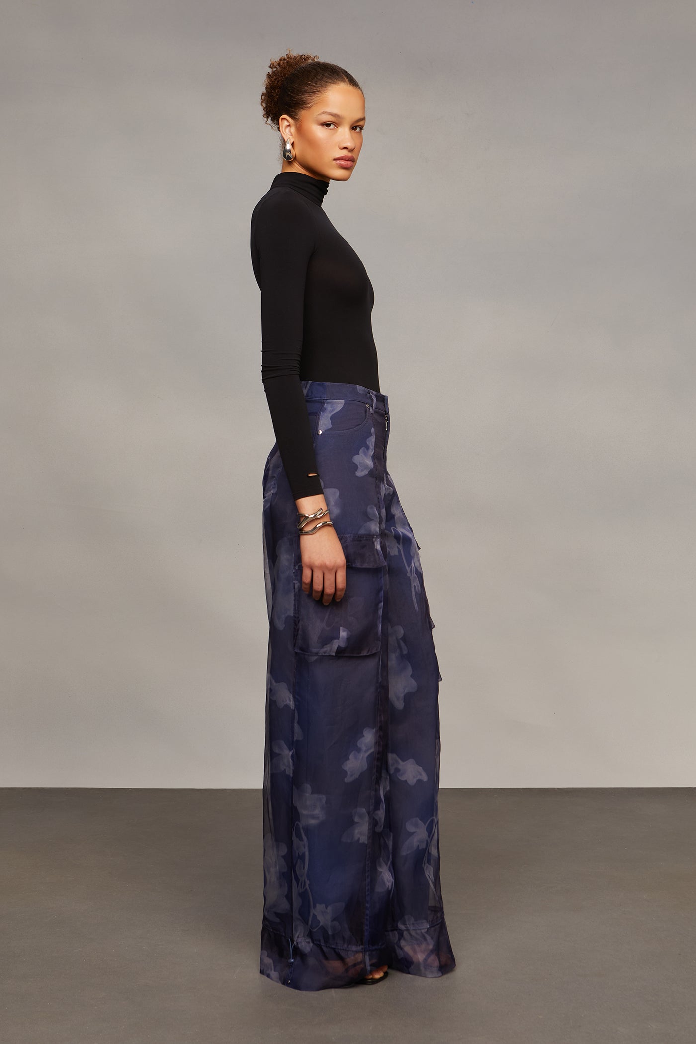 Woman wearing a black top and blue patterned skirt against a gray background