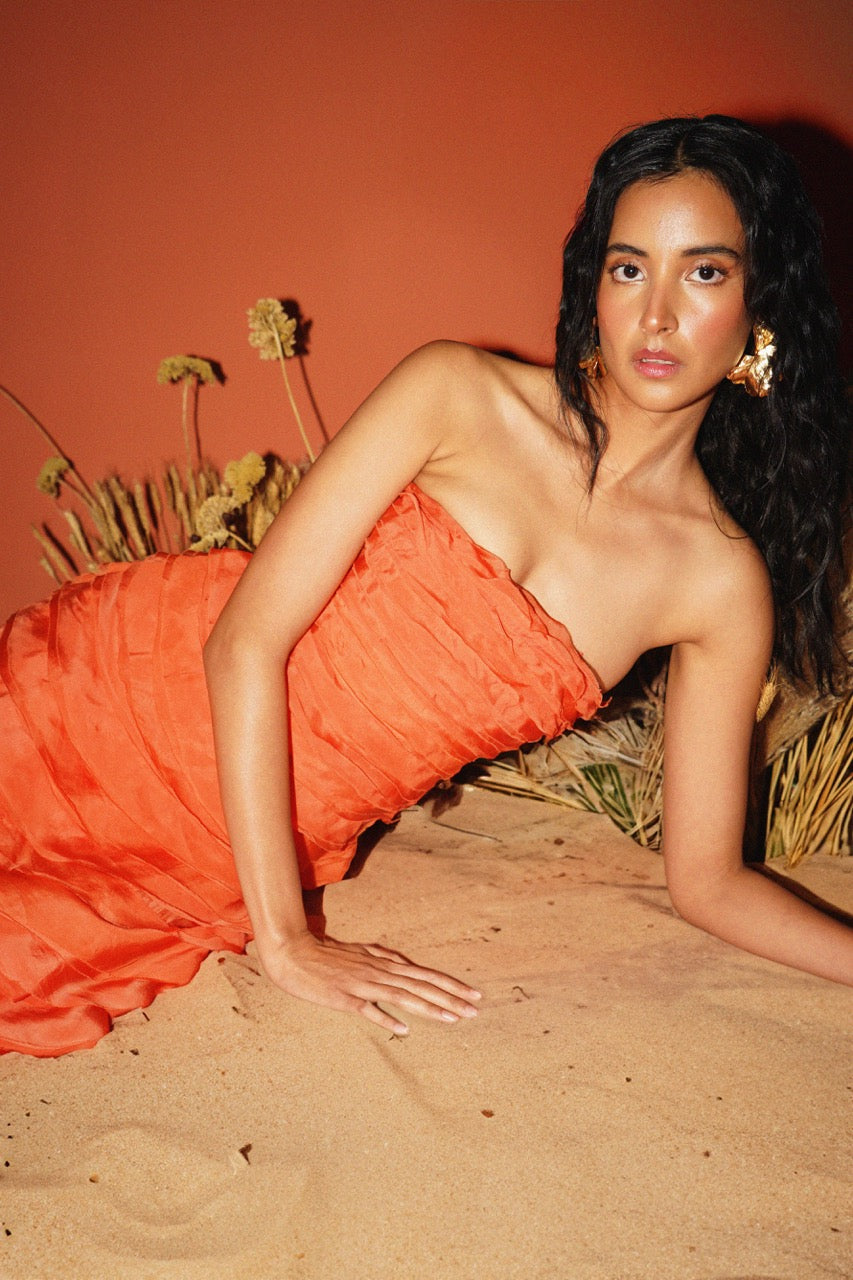 Woman in an orange dress lying on sand with a red background