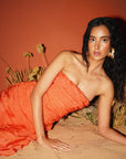 Woman in an orange dress lying on sand with a red background