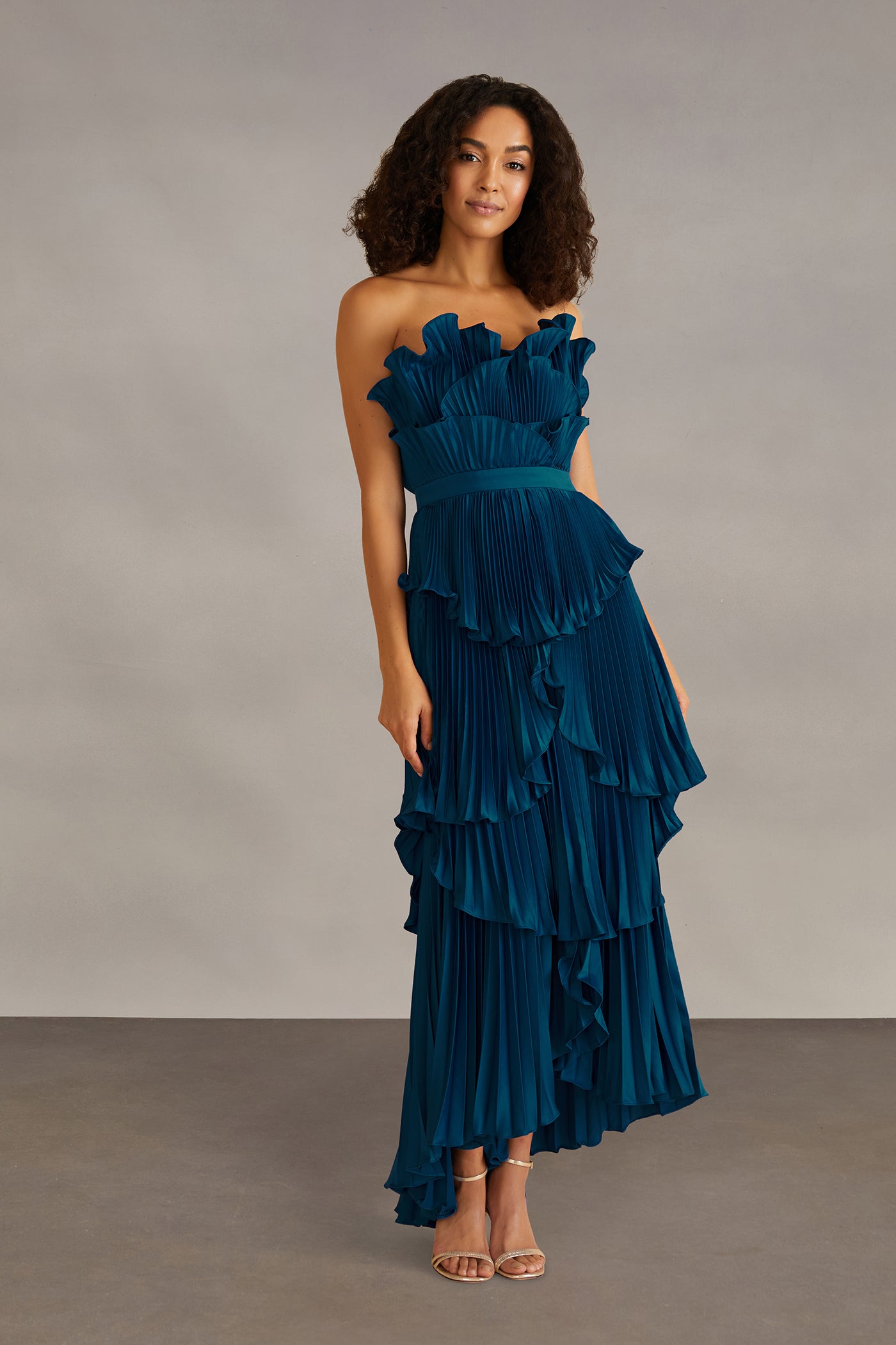 Woman wearing a teal strapless dress with ruffled layers against a neutral background