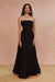 A woman standing in a blush pink pose wearing a black strapless, layered maxi dress.