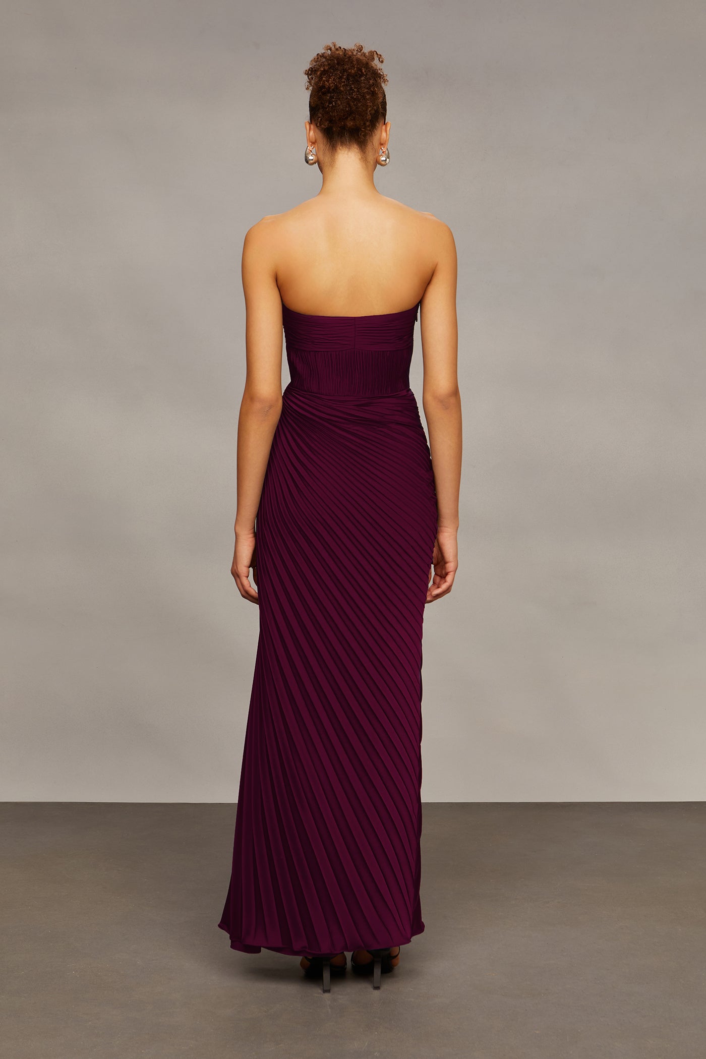 Woman wearing a strapless burgundy gown against a plain background
