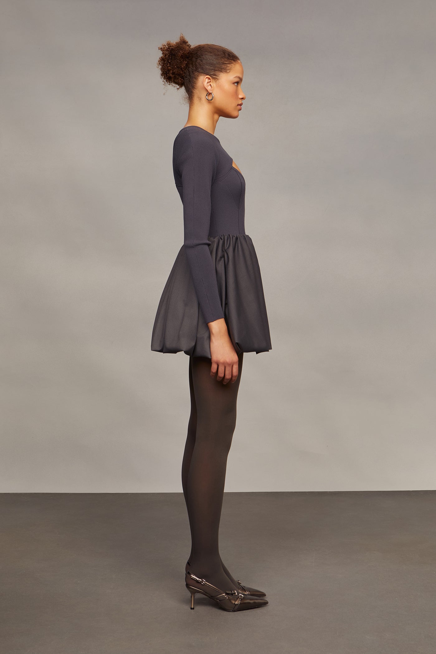 Woman wearing a dark gray dress with a fitted bodice and flared skirt against a plain background