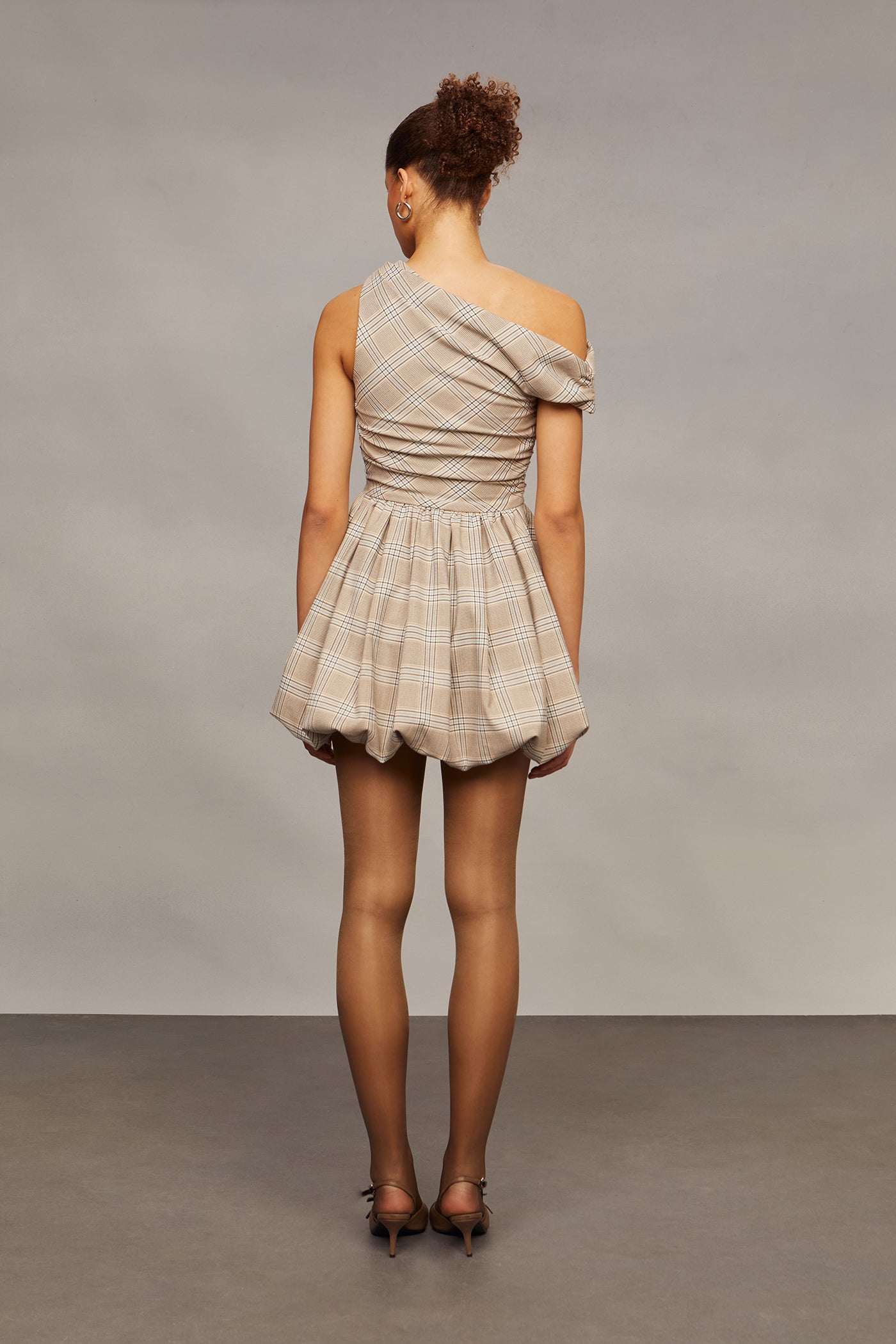 Woman wearing a beige one-shoulder dress against a plain background