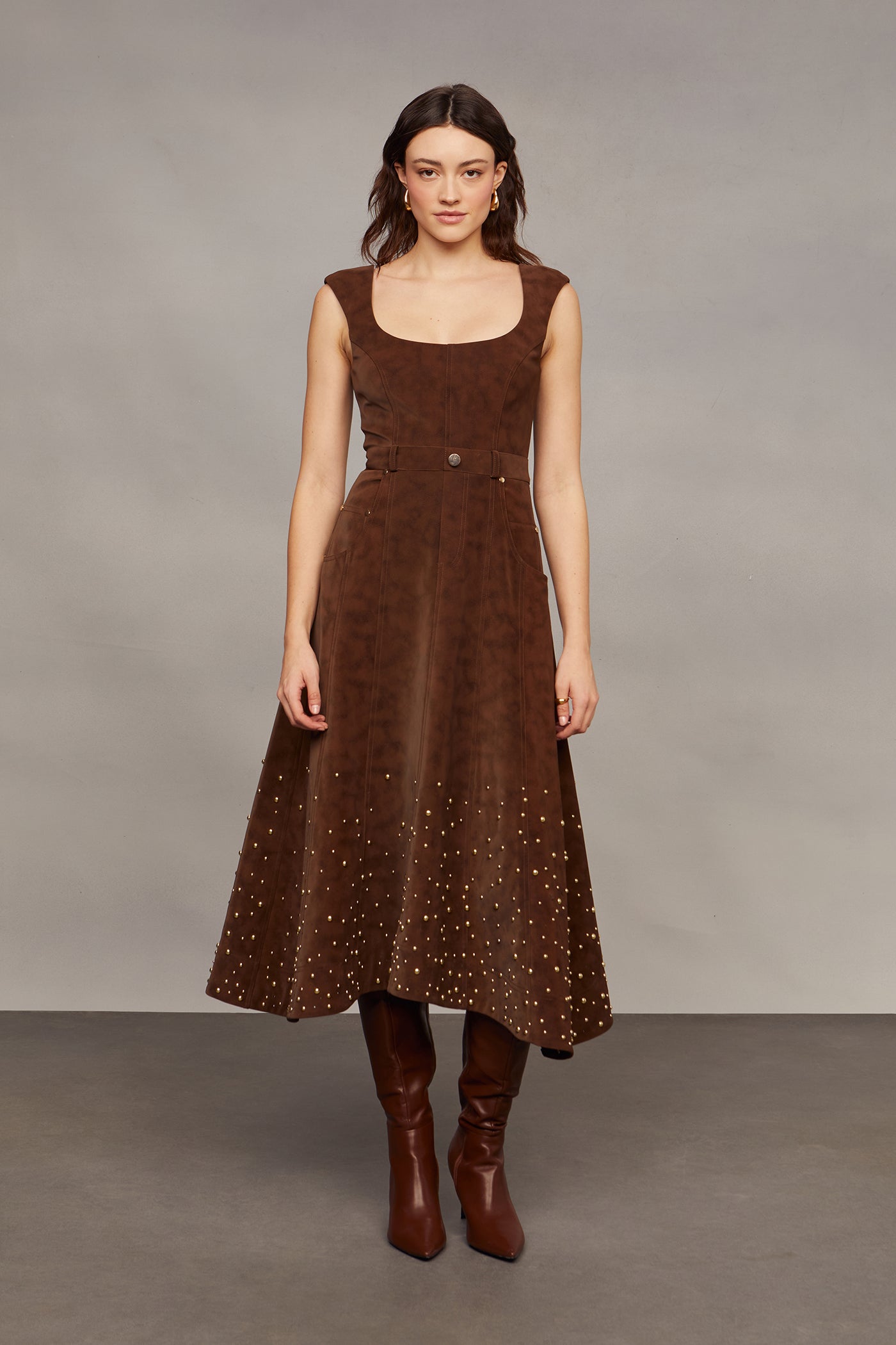 Woman wearing a brown studded dress against a plain background