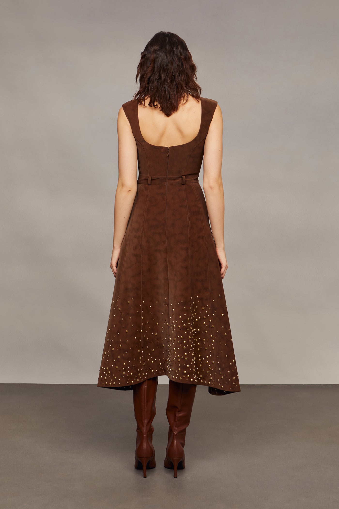Woman wearing a brown studded dress against a plain background