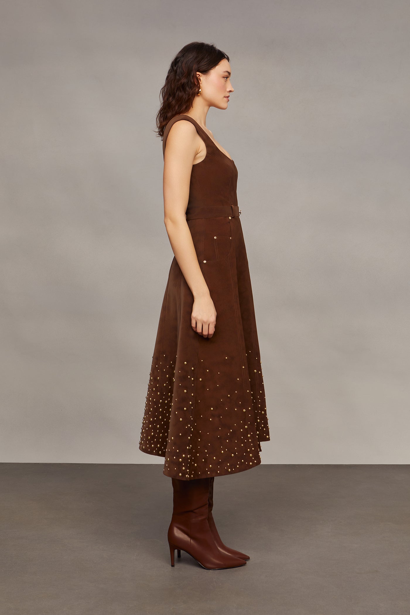 Woman wearing a brown studded dress against a plain background