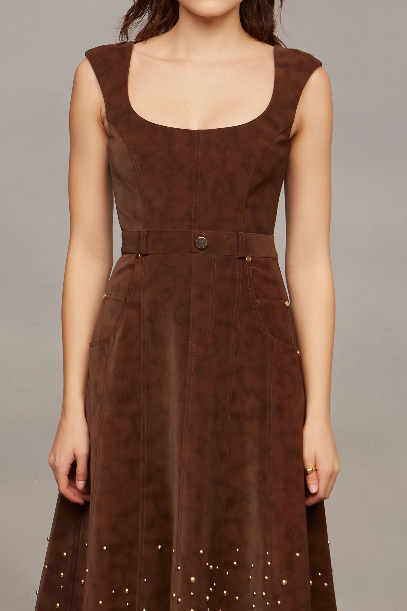 Woman wearing a brown studded dress against a plain background