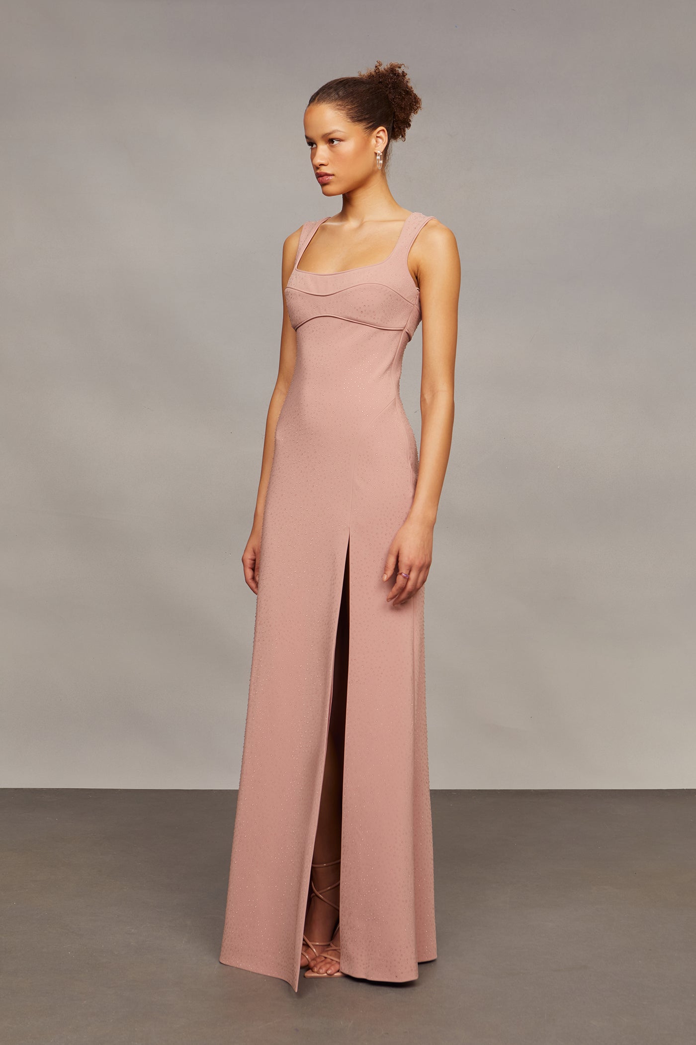 Woman wearing a long pink dress with a slit on a gray background