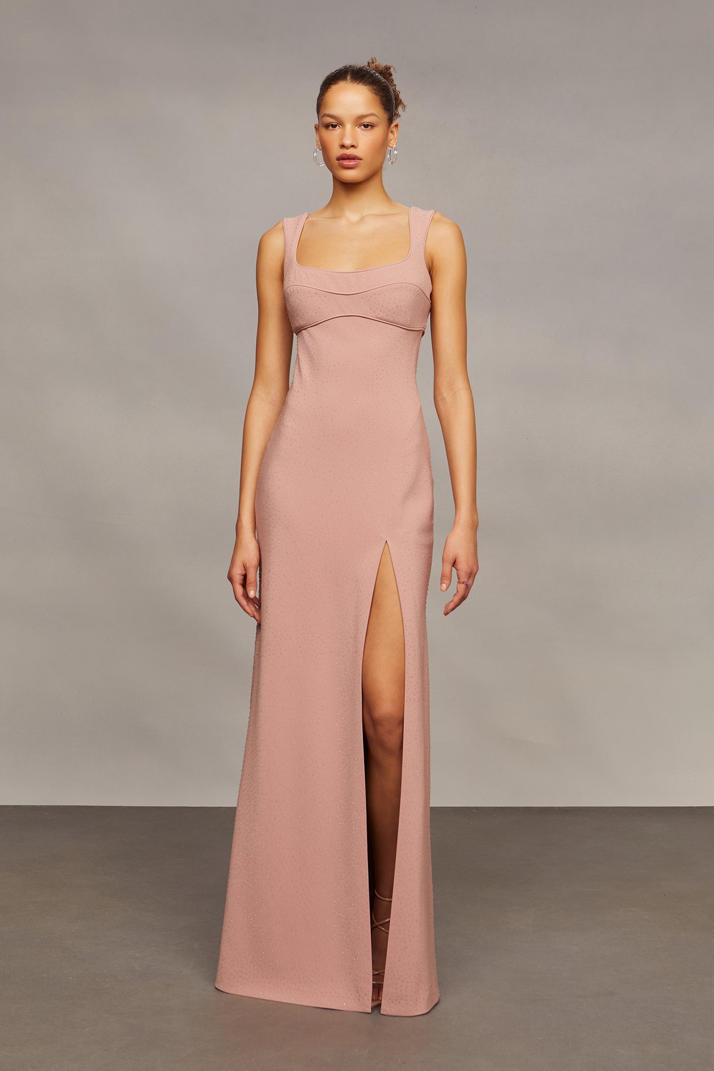 Woman wearing a long, light pink dress with a slit on a neutral background