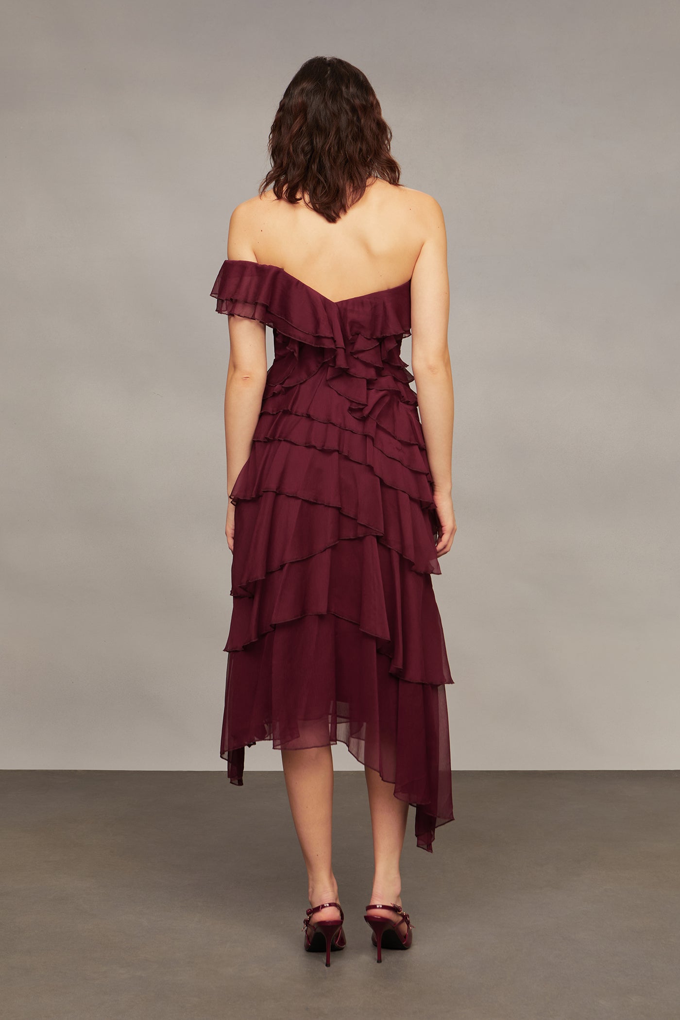 Woman wearing a burgundy off-shoulder dress with ruffled layers on a plain background