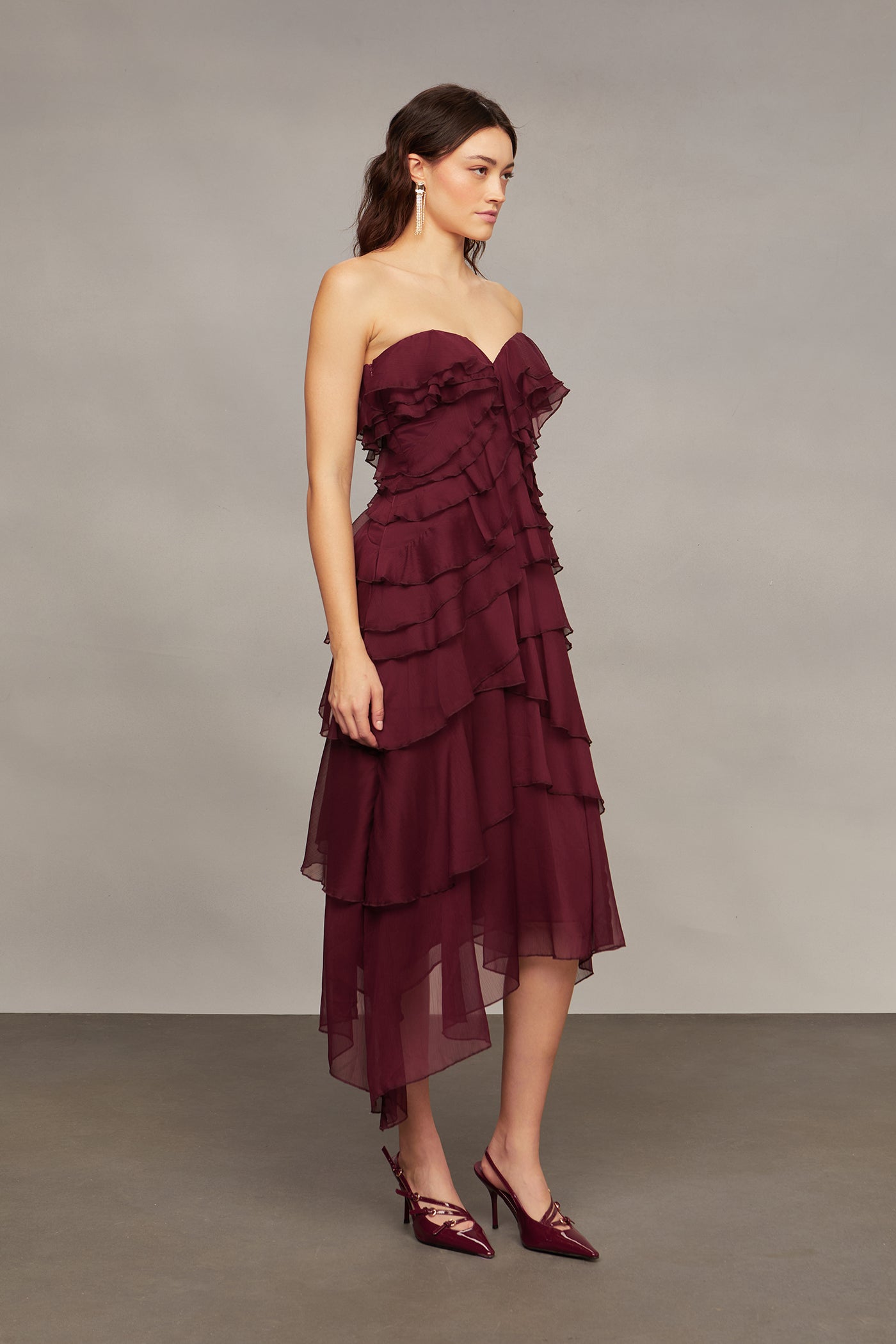 Woman wearing a burgundy strapless dress with ruffled layers on a plain background