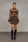 Model wearing a camouflage shirt with sheer sleeves, a matching skirt, and brown knee-high boots on a gray background