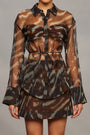 Model wearing a camouflage shirt with sheer sleeves, a matching skirt, and brown knee-high boots on a gray background
