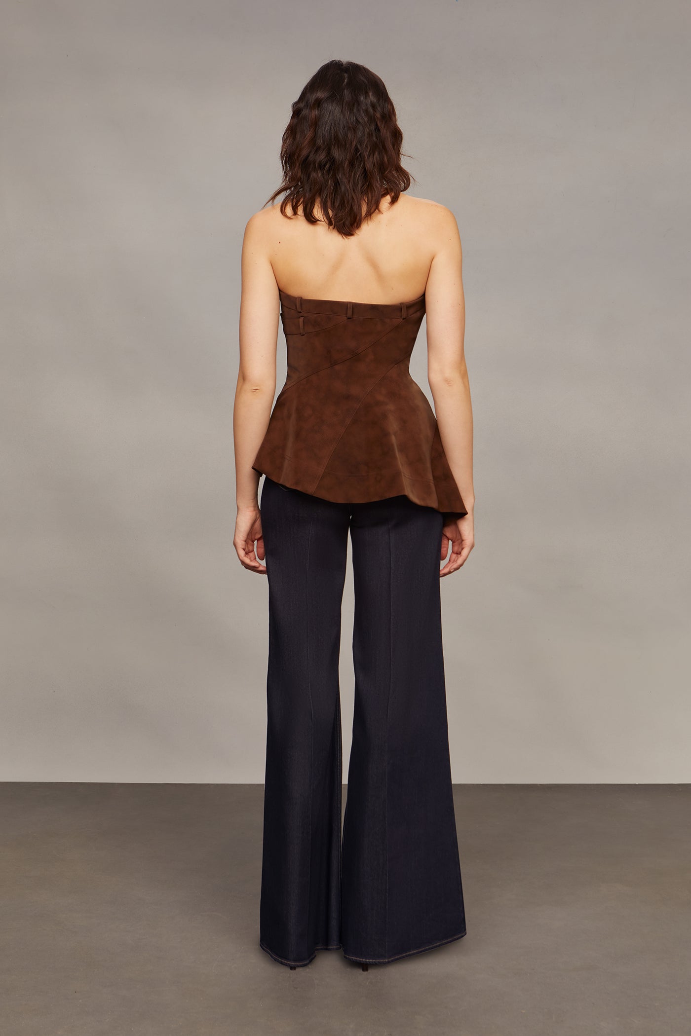 Woman wearing a brown strapless top and blue flared pants against a plain background