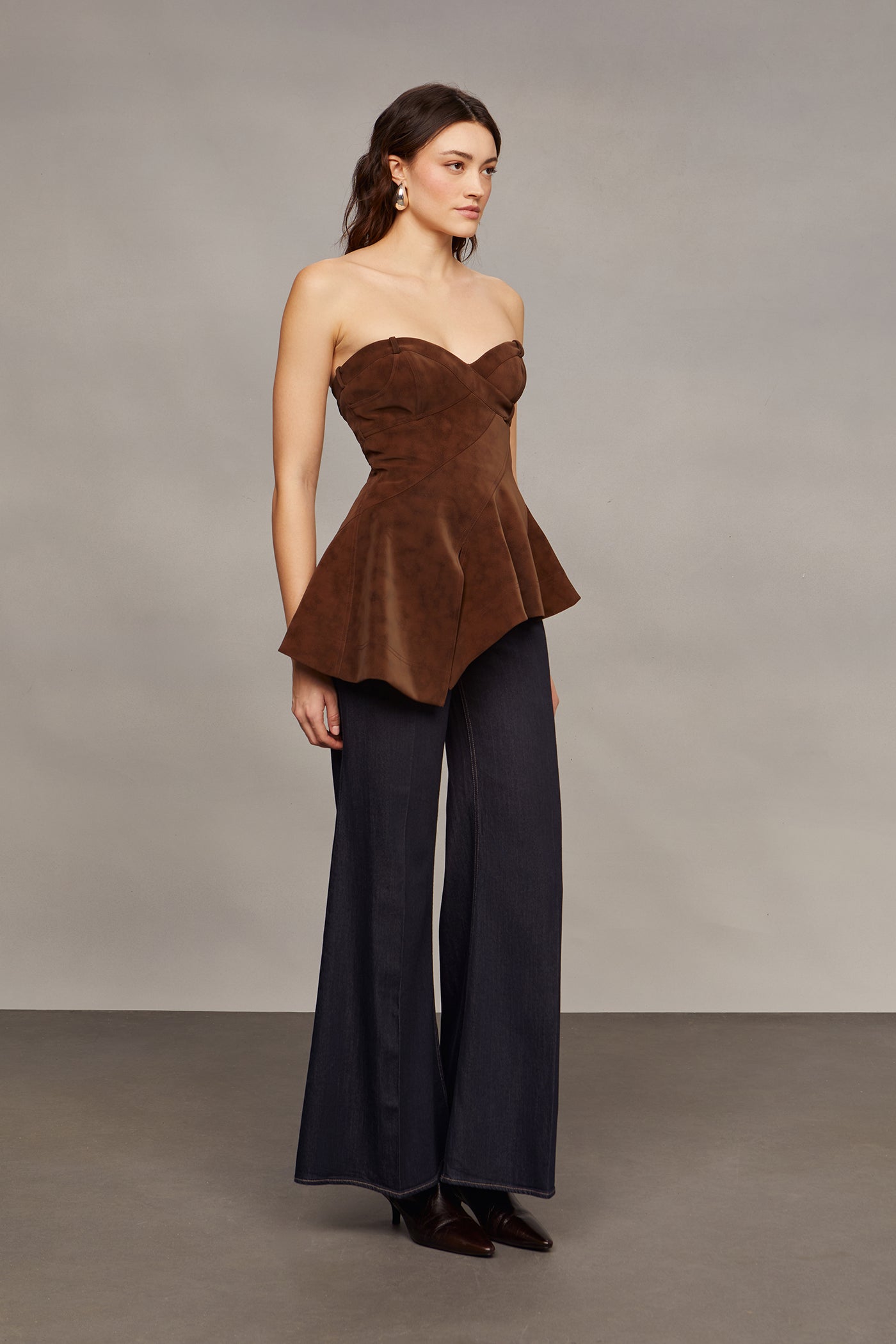 Woman wearing a brown strapless top and blue flared pants against a plain background