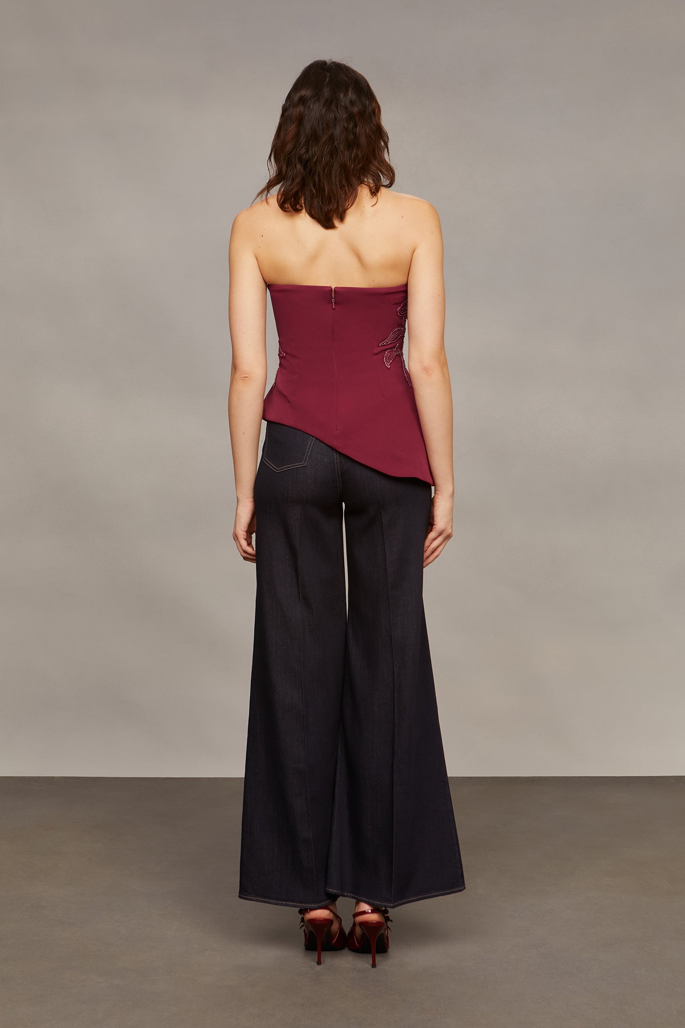 Woman wearing a strapless burgundy top and black wide-leg pants against a plain background