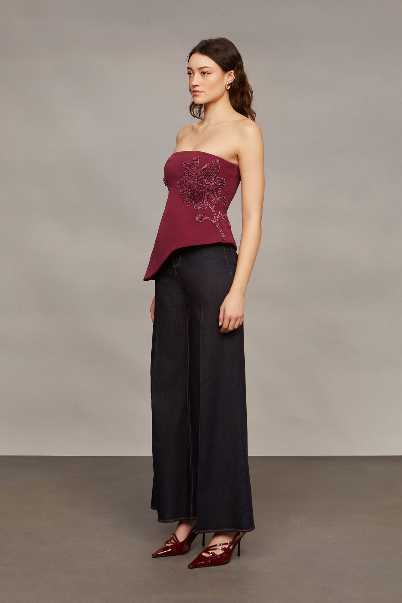 Woman wearing a strapless burgundy top and black pants against a neutral background