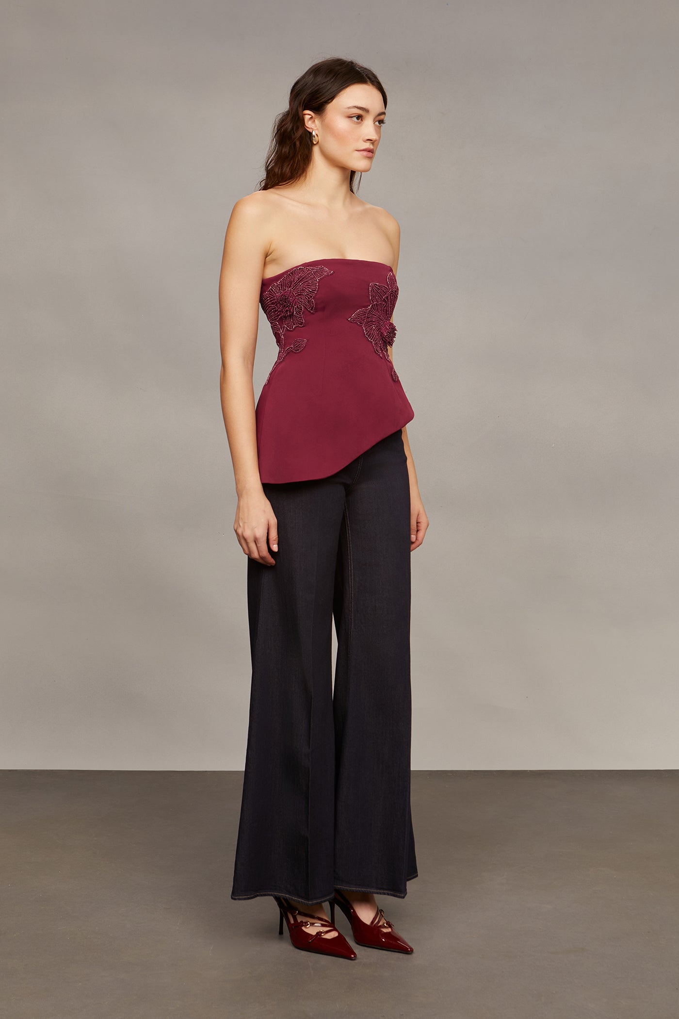 Woman wearing a strapless burgundy top and black pants against a plain background